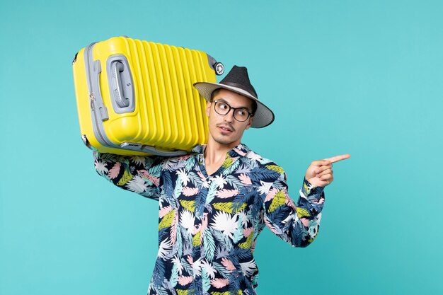 Vorderansicht junger Mann, der in den Urlaub geht und seine gelbe Tasche auf dem blauen Raum hält