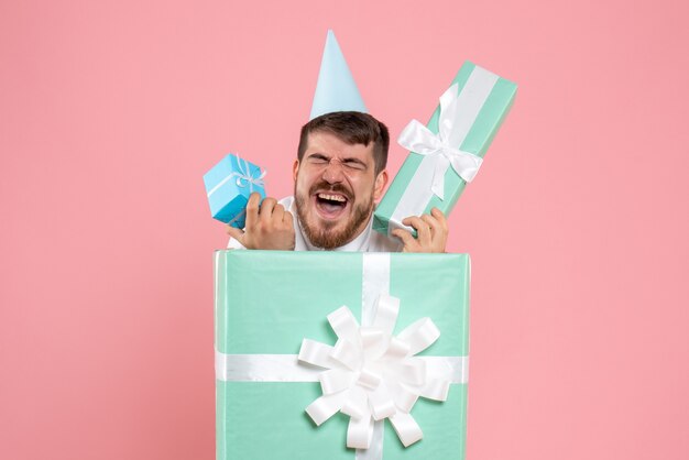 Vorderansicht junger Mann, der innerhalb der gegenwärtigen Box auf rosa Schreibtischfarbpyjama-Partyfoto-Emotionsschlafweihnachten steht