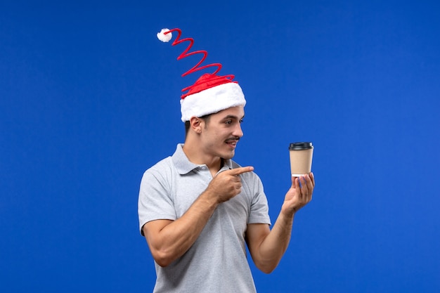 Vorderansicht junger Mann, der Kaffeetasse an der blauen Wand Neujahrsfeiertag hält