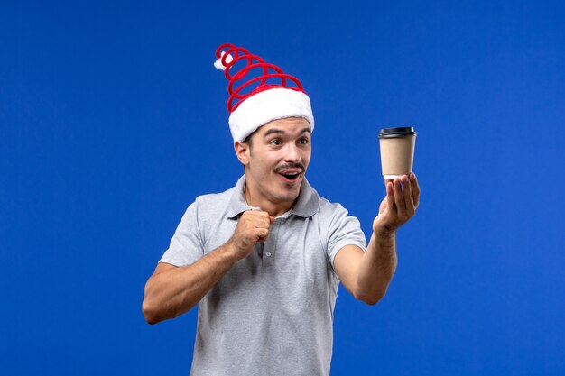Vorderansicht junger Mann, der Kaffeetasse auf männlicher Feiertagsemotion der blauen Wand des neuen Jahres hält