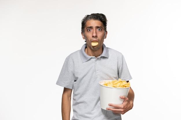 Vorderansicht junger Mann, der Kartoffelchips hält und Film auf weißer Oberfläche sieht