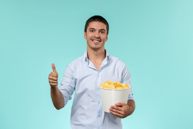 Vorderansicht junger Mann, der Kartoffelspitzen mit Lächeln auf einem einsamen entfernten männlichen Filmkino der blauen Wand hält