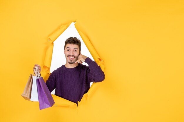 Vorderansicht junger Mann, der kleine Pakete nach dem Einkaufen auf gelbem Hintergrund hält Modell Geschenk Neujahr präsentiert Weihnachtsfarbe