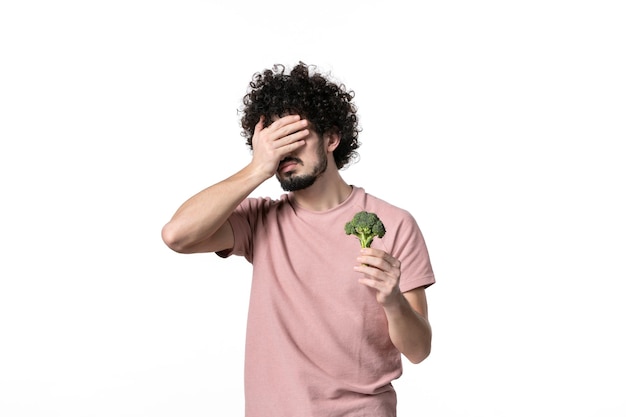 Vorderansicht junger Mann, der kleinen grünen Brokkoli auf weißem Hintergrund hält Körpergesundheit horizontales Gewicht Gemüse menschliche Salatdiät