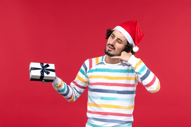 Vorderansicht junger Mann, der kleines Geschenk am roten Wand-Emotionsfeiertag Silvester hält