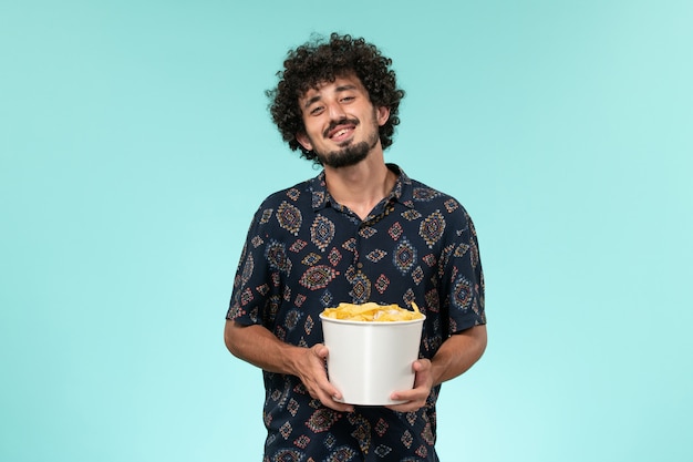 Vorderansicht junger Mann, der Korb mit Cips auf dem ferngesteuerten Kinofilm des blauen Hintergrunds hält