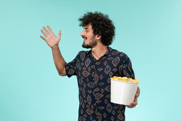 Vorderansicht junger Mann, der Korb mit Cips auf einem entfernten Filmfilm der blauen Wand fernhält