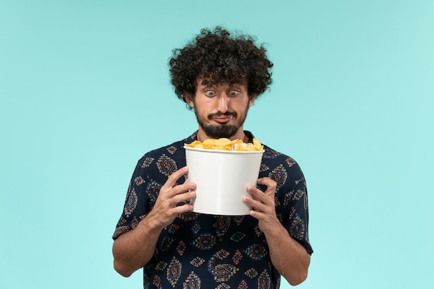 Vorderansicht junger Mann, der Korb mit Cips auf einem entfernten Wandkino des blauen Wandfilmkinos hält