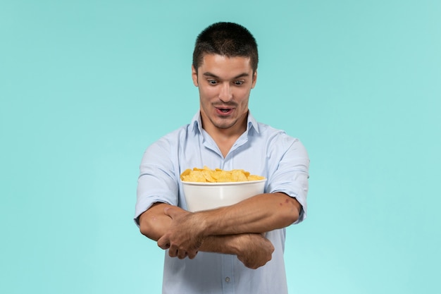 Vorderansicht junger Mann, der Korb mit Cips auf ferngesteuertem Filmkino-Männchen des blauen Wandfilms fernhält