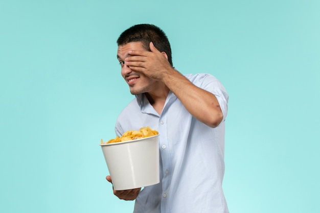 Vorderansicht junger mann, der korb mit kartoffelchips hält und film auf blauer oberfläche sieht