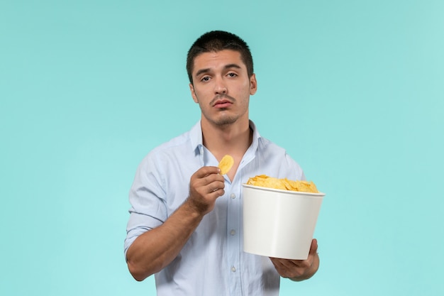 Kostenloses Foto vorderansicht junger mann, der korb mit kartoffelspitzen auf hellblauem wandfilmfernfilmkino hält