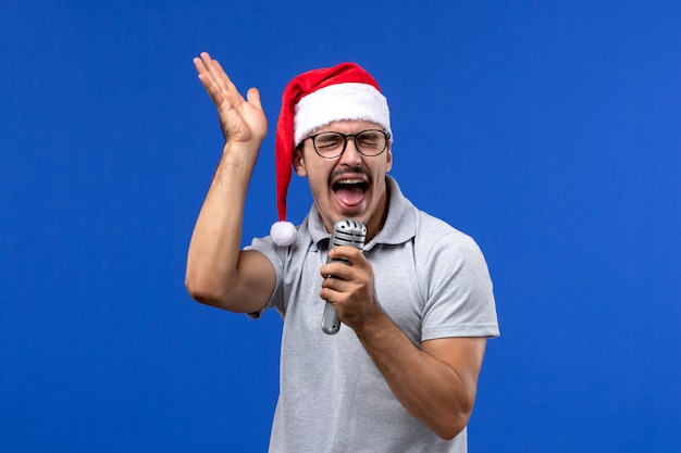 Vorderansicht junger Mann, der Mikrofon auf blauer Wand Neujahrsmusik-Sänger hält