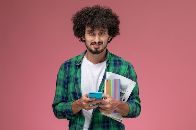 Vorderansicht junger Mann, der mit Handy und Notizbüchern auf rotem Hintergrund aufwirft