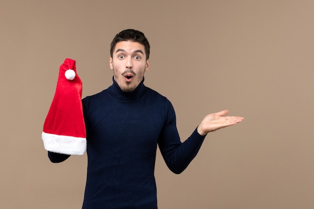 Vorderansicht junger Mann, der mit roter Kappe auf braunem Hintergrundweihnachtsemotionsfeiertag spielt