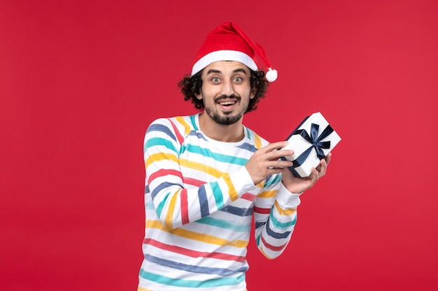 Vorderansicht junger Mann, der Neujahrsgeschenk auf roten Hintergrundfeiertagsneujahrsemotionen hält