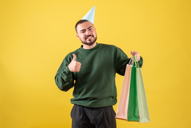 Vorderansicht junger Mann, der Pakete mit Geschenken auf gelbem Hintergrund hält