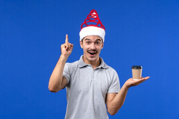 Vorderansicht junger Mann, der Plastikkaffeetasse auf einem blauen Schreibtisch Emotionen Neujahrsmann hält