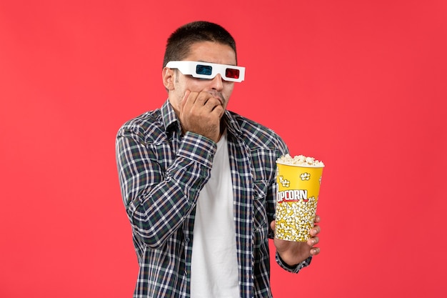 Vorderansicht junger Mann, der Popcorn in d Sonnenbrille auf der hellroten Wand männlicher Kino-Kinofilm hält