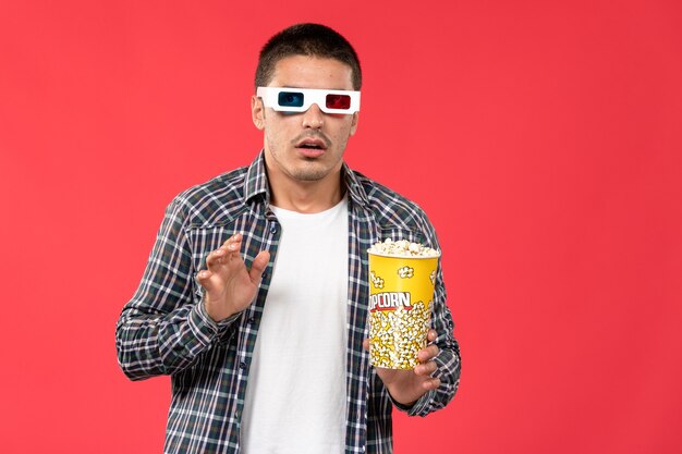 Vorderansicht junger Mann, der Popcorn in d Sonnenbrille auf der hellroten Wand männlicher Kino-Kinofilm hält