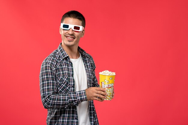 Vorderansicht junger Mann, der Popcorn in -d Sonnenbrille auf der roten Wand Kino Kino Film hält