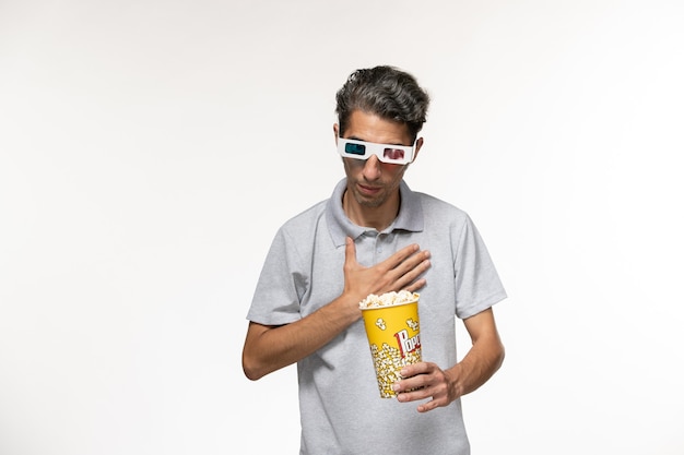Vorderansicht junger Mann, der Popcorn-Paket in d Sonnenbrille auf der weißen Oberfläche hält