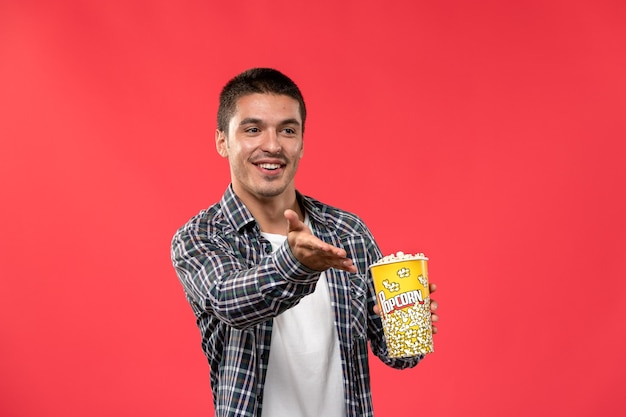 Vorderansicht junger Mann, der Popcornpaket auf dem männlichen Film des hellroten Wandkino-Theaterfilms hält