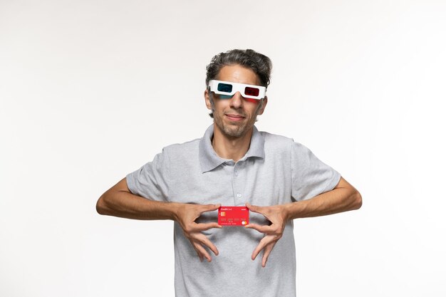 Vorderansicht junger Mann, der rote Bankkarte in d Sonnenbrille auf weißem Schreibtisch hält