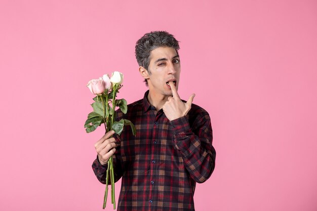 Vorderansicht junger Mann, der schöne rosa Rosen am Tag der Frauen an rosa Wand hält