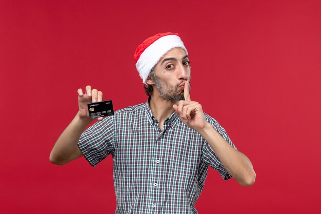 Vorderansicht junger Mann, der schwarze Bankkarte auf dem roten Hintergrund hält