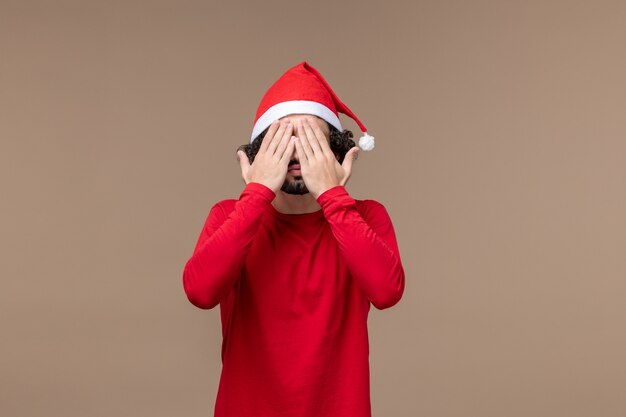 Vorderansicht junger Mann, der sein Gesicht auf braunem Hintergrundweihnachtsgefühlfeiertag bedeckt