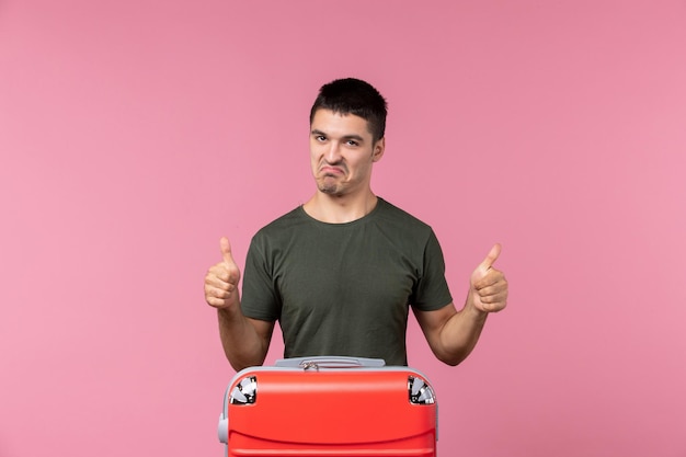 Vorderansicht junger Mann, der sich auf den Urlaub mit großer Tasche auf dem rosafarbenen Raum vorbereitet