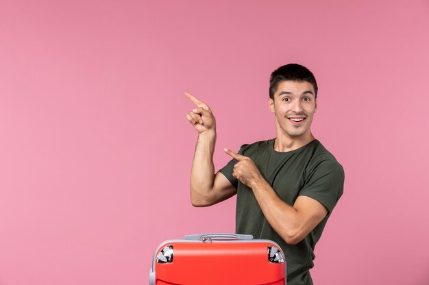 Vorderansicht junger Mann, der sich auf den Urlaub vorbereitet, mit großer Tasche, die auf rosafarbenem Raum lächelt