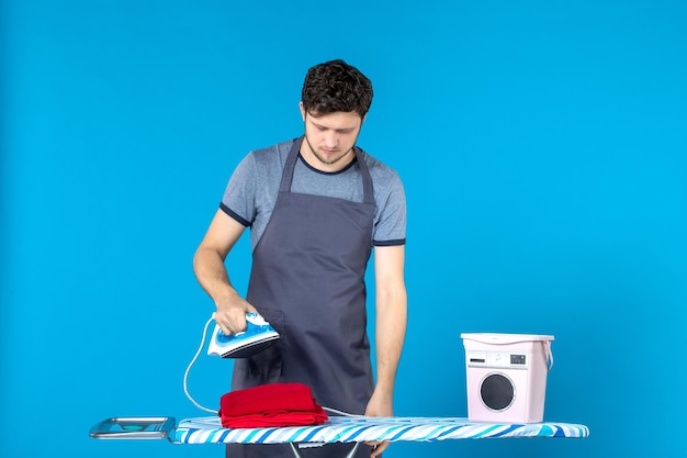 Kostenloses Foto vorderansicht junger mann, der sich darauf vorbereitet, auf blauem hintergrund zu bügeln, kleidung, waschmaschine, reinigung, bügeleisen, wäsche, hausarbeit