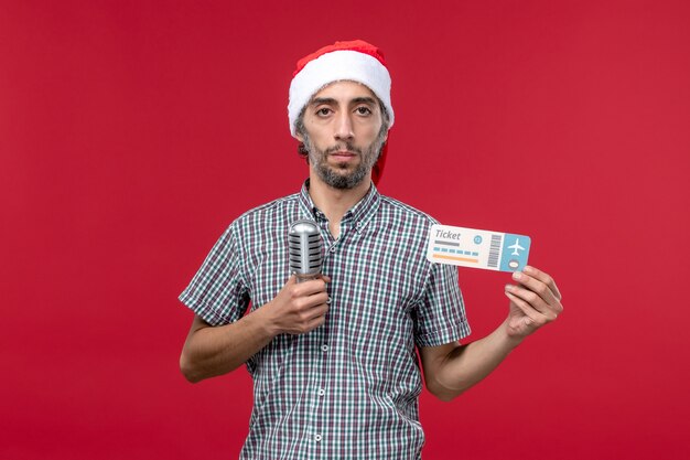 Vorderansicht junger Mann, der Ticket mit Mikrofon auf rotem Hintergrund hält