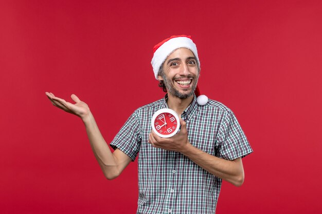 Vorderansicht junger Mann, der Uhren mit lächelndem Ausdruck auf roter Wand roter Emotionszeit hält