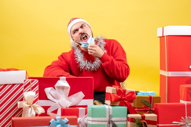 Vorderansicht junger Mann, der um Geschenke auf gelbem Hintergrund sitzt