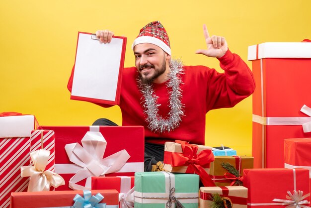 Vorderansicht junger Mann, der um Geschenke auf gelbem Hintergrund sitzt