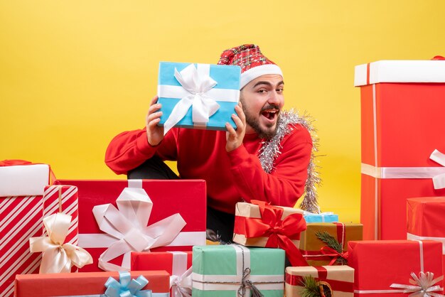 Vorderansicht junger Mann, der um Geschenke auf gelbem Hintergrund sitzt