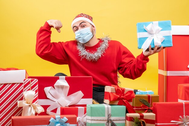 Vorderansicht junger Mann, der um Geschenke auf gelbem Hintergrund sitzt