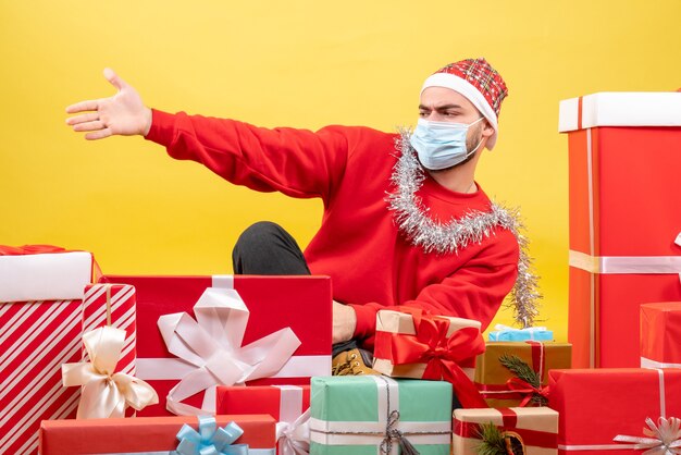 Vorderansicht junger Mann, der um Geschenke auf gelbem Hintergrund sitzt