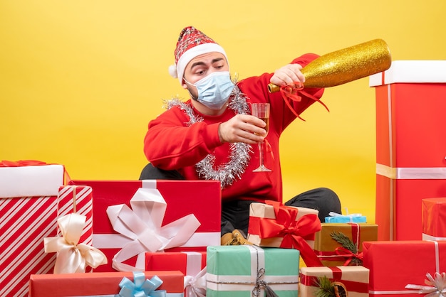 Vorderansicht junger Mann, der um Geschenke auf gelbem Hintergrund sitzt