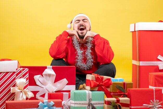 Vorderansicht junger Mann, der um Geschenke auf gelbem Hintergrund sitzt