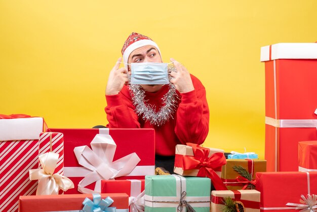 Vorderansicht junger Mann, der um Geschenke auf gelbem Hintergrund sitzt