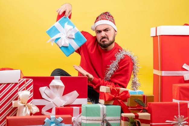 Vorderansicht junger Mann, der um Geschenke sitzt und eins auf gelbem Hintergrund hält