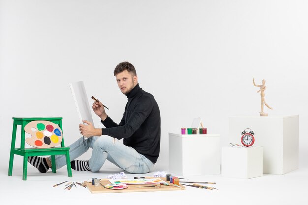 Vorderansicht junger Mann, der versucht, Gemälde mit Quaste auf weißer Wand zu zeichnen Farbbild malen Kunst malen Zeichnungen Künstler