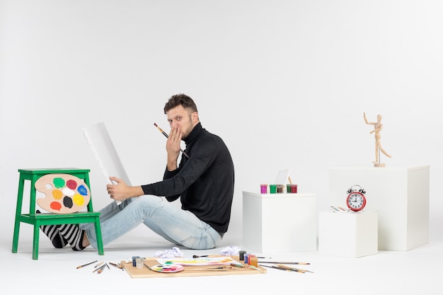 Vorderansicht junger Mann, der versucht, Gemälde mit Quaste auf weißer Wand zu zeichnen