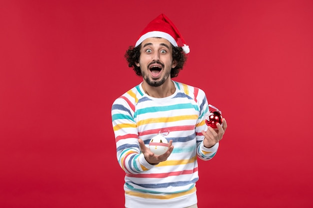 Vorderansicht junger Mann, der Weihnachtsbaumspielzeug auf menschlichem Neujahr des Feiertags der roten Wand hält