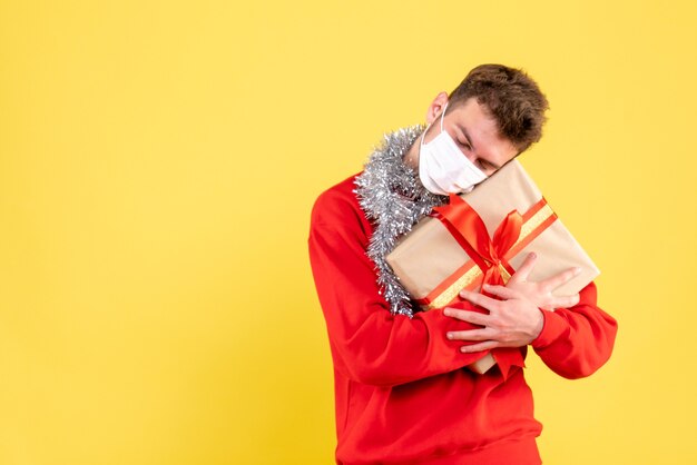 Vorderansicht junger Mann, der Weihnachtsgeschenk in der sterilen Maske hält