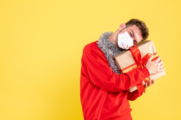 Vorderansicht junger Mann, der Weihnachtsgeschenk in der sterilen Maske hält