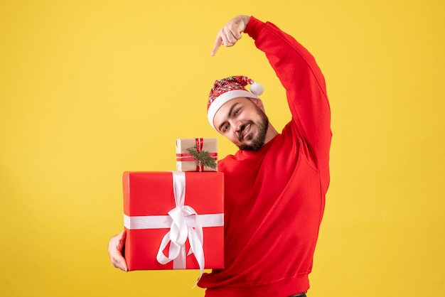 Vorderansicht junger Mann, der Weihnachtsgeschenke auf einem gelben Hintergrund hält